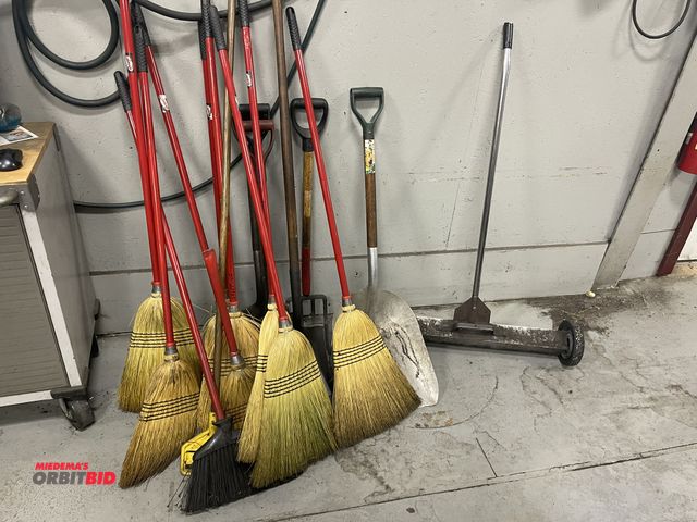 Lot 1-19526 - Lot of assorted hand tools, includes (7) brooms, (5) square shovels, (1) scoop shovel, and (1) 30" m...