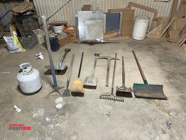 Lot 1-11606 - Lot of assorted rakes, shovels, brooms, tamper, propane tank, and scoop shovel.