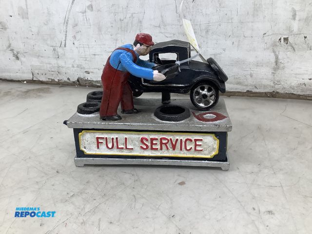 Lot 2-56996 - cast iron mechanical bank. man changing tire of oil and dumps coin under car. 6 x 7 inches