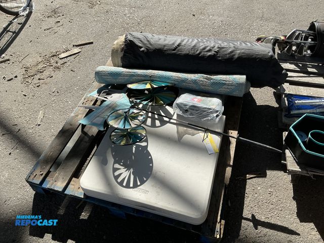 Lot 2-55604 - Skid of assorted items including a folding table, tarp, tractor decor and 3 camp rugs. 72”x36”. Dark...