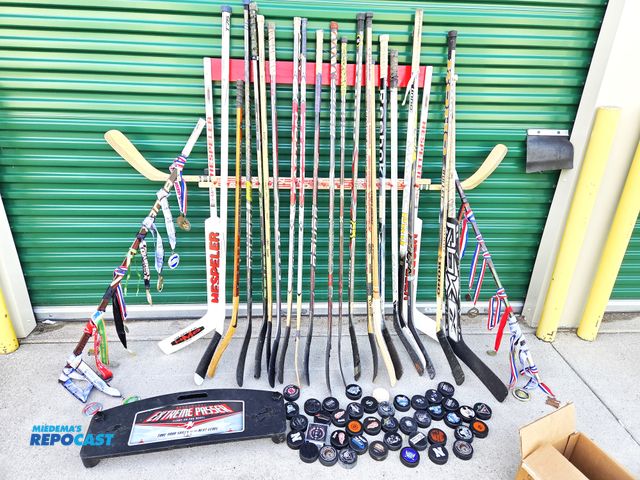 Lot 2-94305 - Hockey stick display with 21 game-used sticks, pucks, and tons of tournament medals.