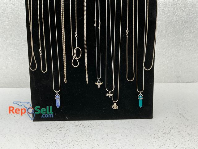 Lot 31-1420 - Twelve necklaces displayed on a black stand. Includes various chain styles and pendant designs, such...