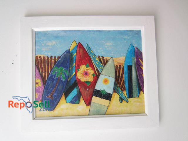 Lot 31-9202 - Framed artwork depicting colorful surfboards standing upright against a sandy background with a wood...
